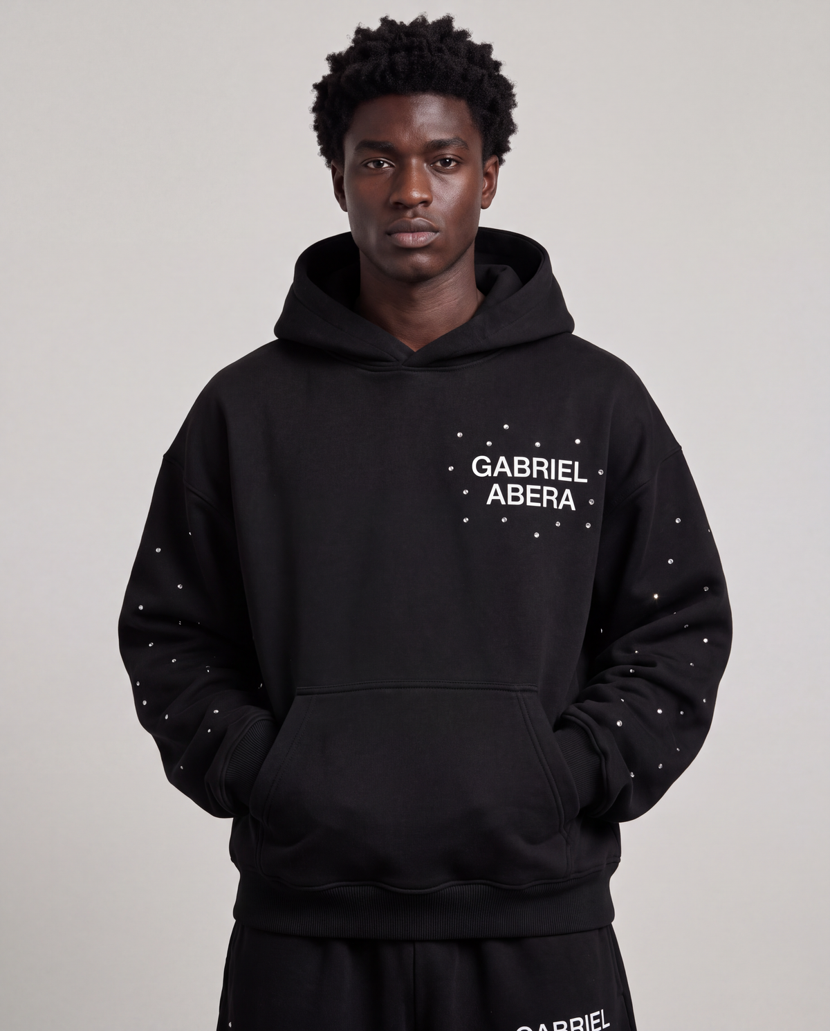 Model trägt den schwarzen GABRIEL ABERA Rhinestone Astral Hoodie mit auffälligem Astral-Rhinestone-Design und Oversized Fit