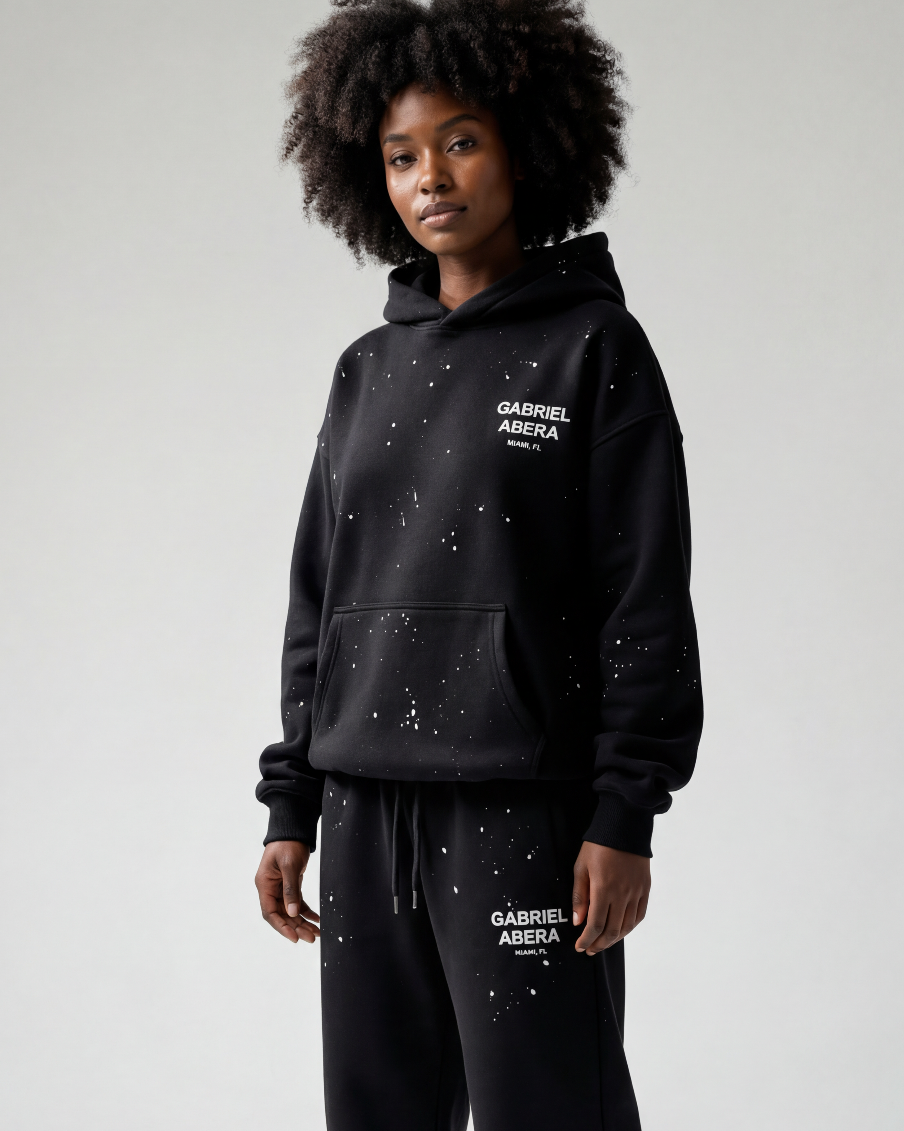 Schwarzes weibliches Model trägt den GABRIEL ABERA Hoodie in Schwarz im Oversized Streetwear Fit, Frontansicht.