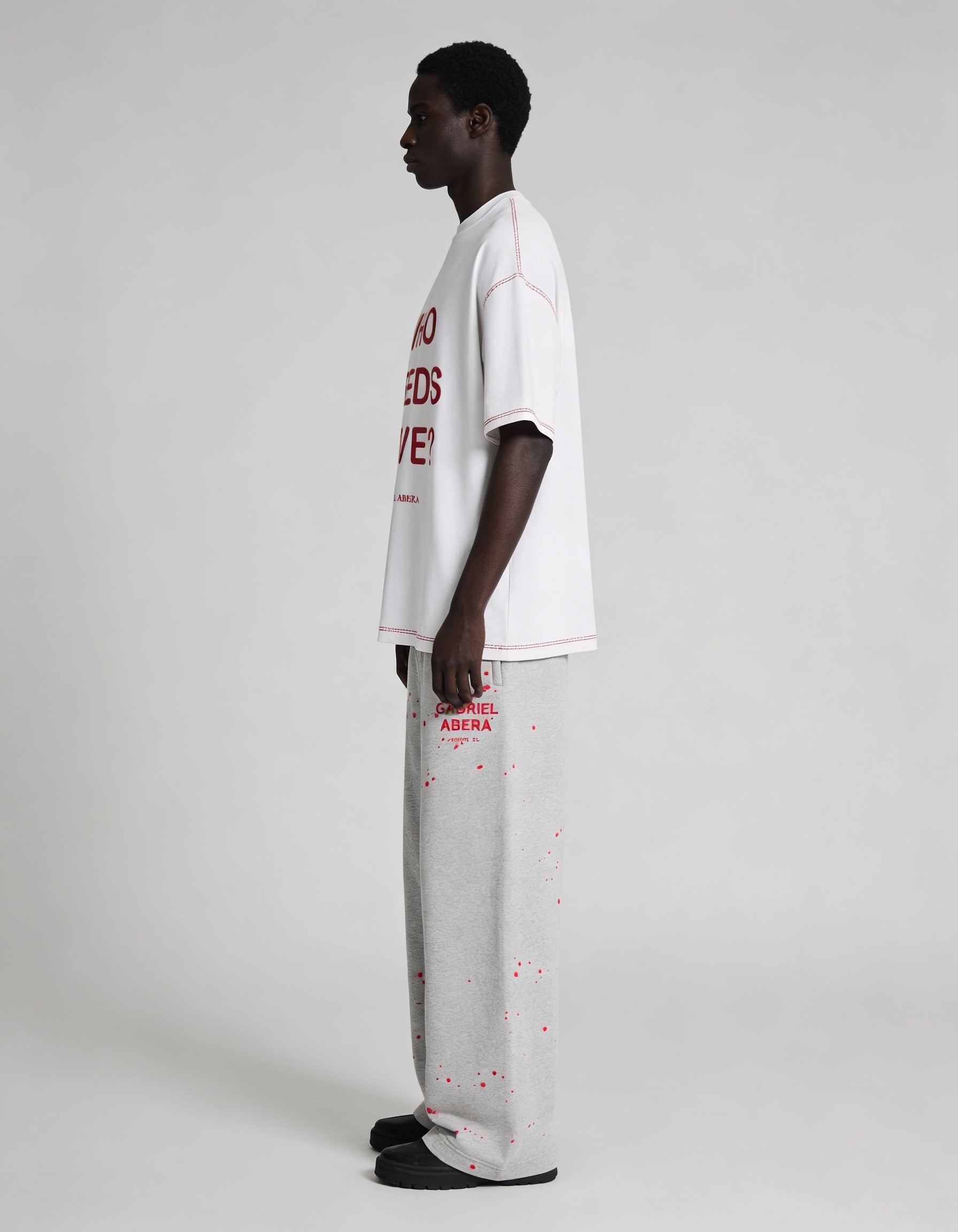 Seitliche Ansicht des weißen GABRIEL ABERA WHO NEEDS LOVE T-Shirts auf männlichem Model, Oversized Passform und klarer Stofffall