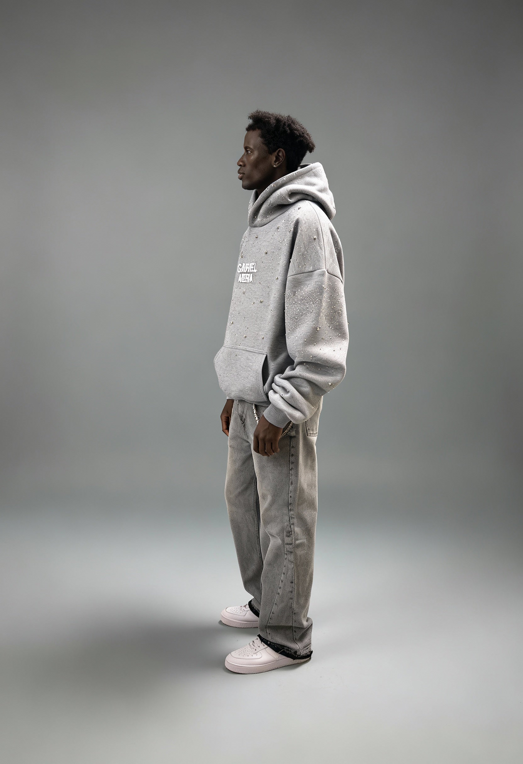 Grauer GABRIEL ABERA Universe Hoodie – männliches Model seitlich fotografiert, Oversized Silhouette mit funkelnden Rhinestones sichtbar.