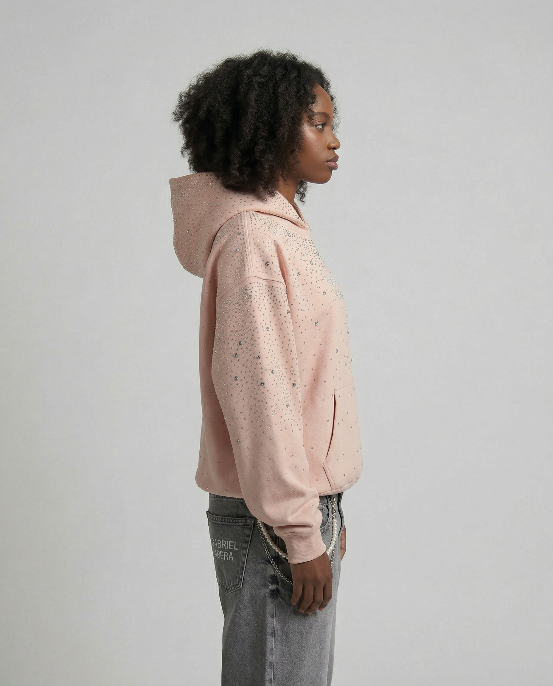 Female model side view GABRIEL ABERA pink rhinestone hoodie oversized silhouette clean streetwear styling with rhinestone details