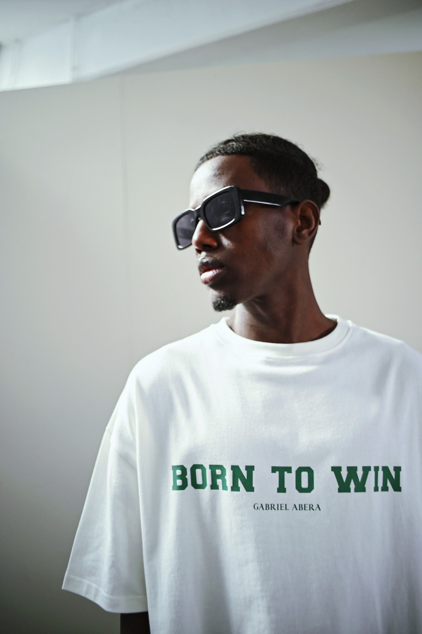 Model trägt das weiße T-shirt mit grünem "Born 2 Win" Druck auf der Brust