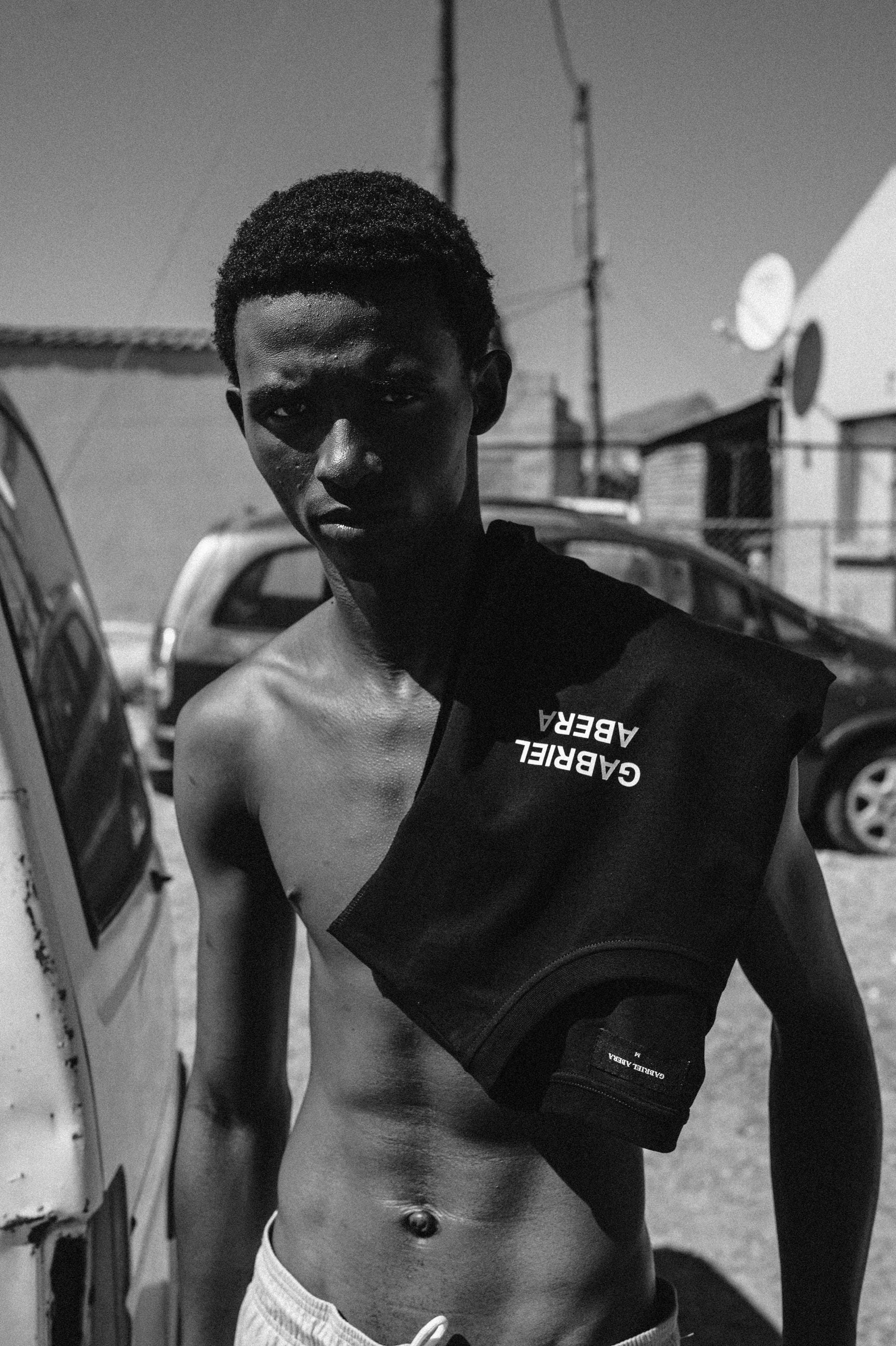 Model in GABRIEL ABERA Tanktop vor Wellblechhütte in Lwandle.