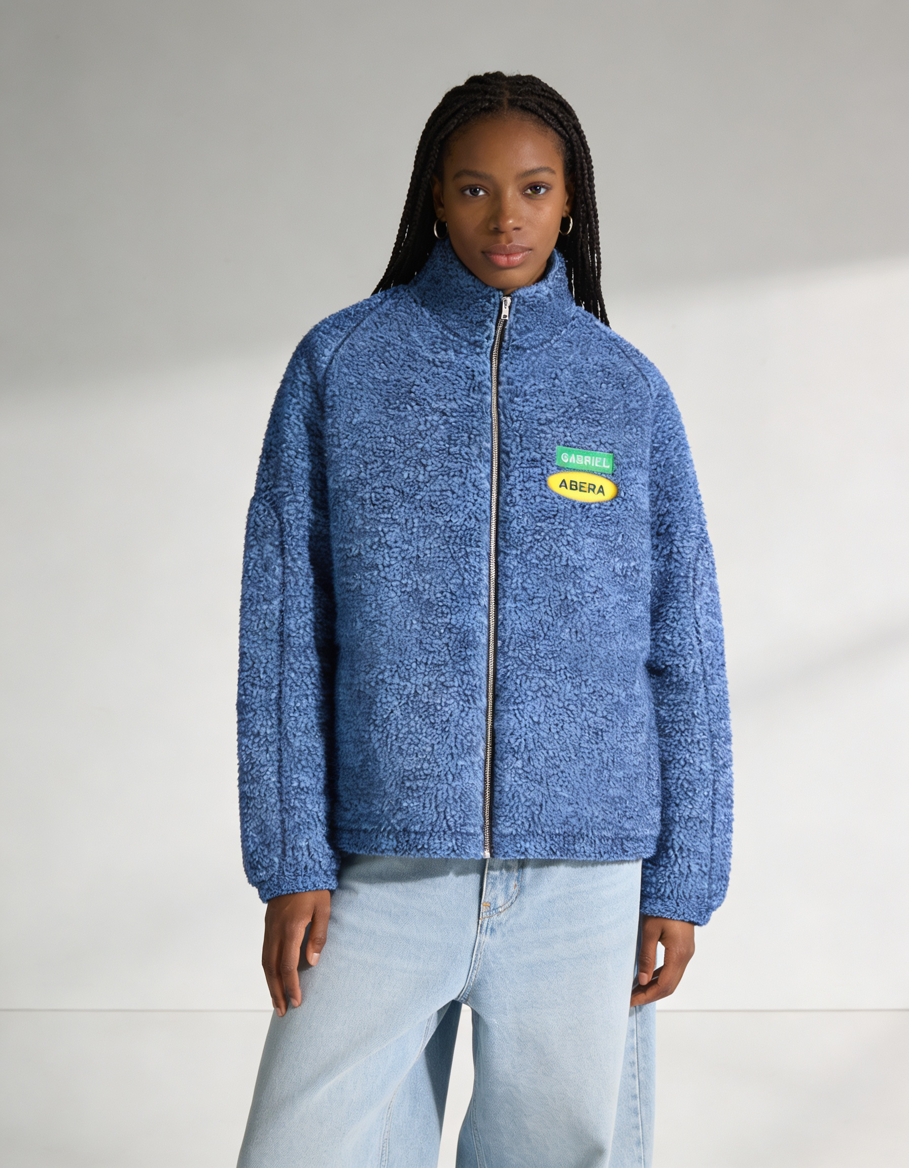 Female model wearing the blue fleece jacket by GABRIEL ABERA from the front, cozy textured fleece, relaxed unisex streetwear style.