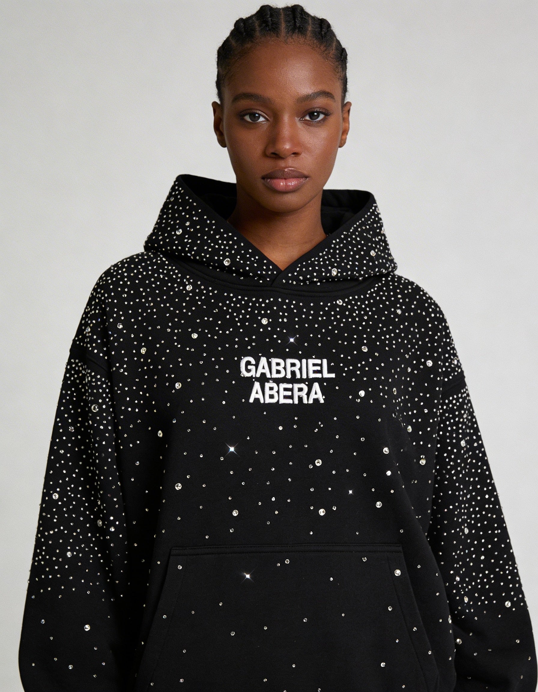 Weibliches Model in schwarzem GABRIEL ABERA Rhinestone Hoodie – Frontansicht, elegante Rhinestone-Applikation, Urban Streetwear Fit.