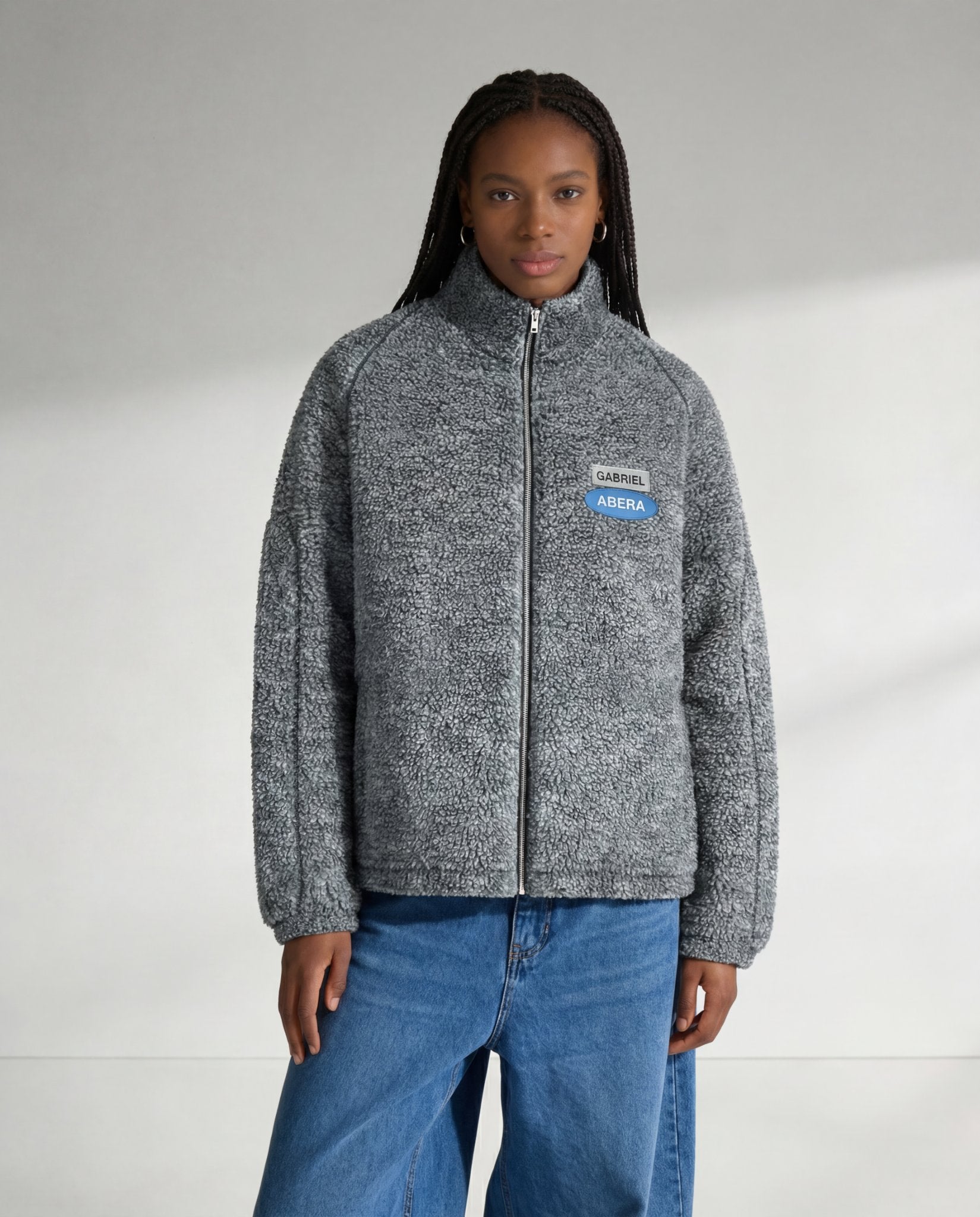 Graue GABRIEL ABERA Fleecejacke auf weiblichem Model von vorne, Streetwear Look mit weichem Fleece-Material und Logo-Patch.