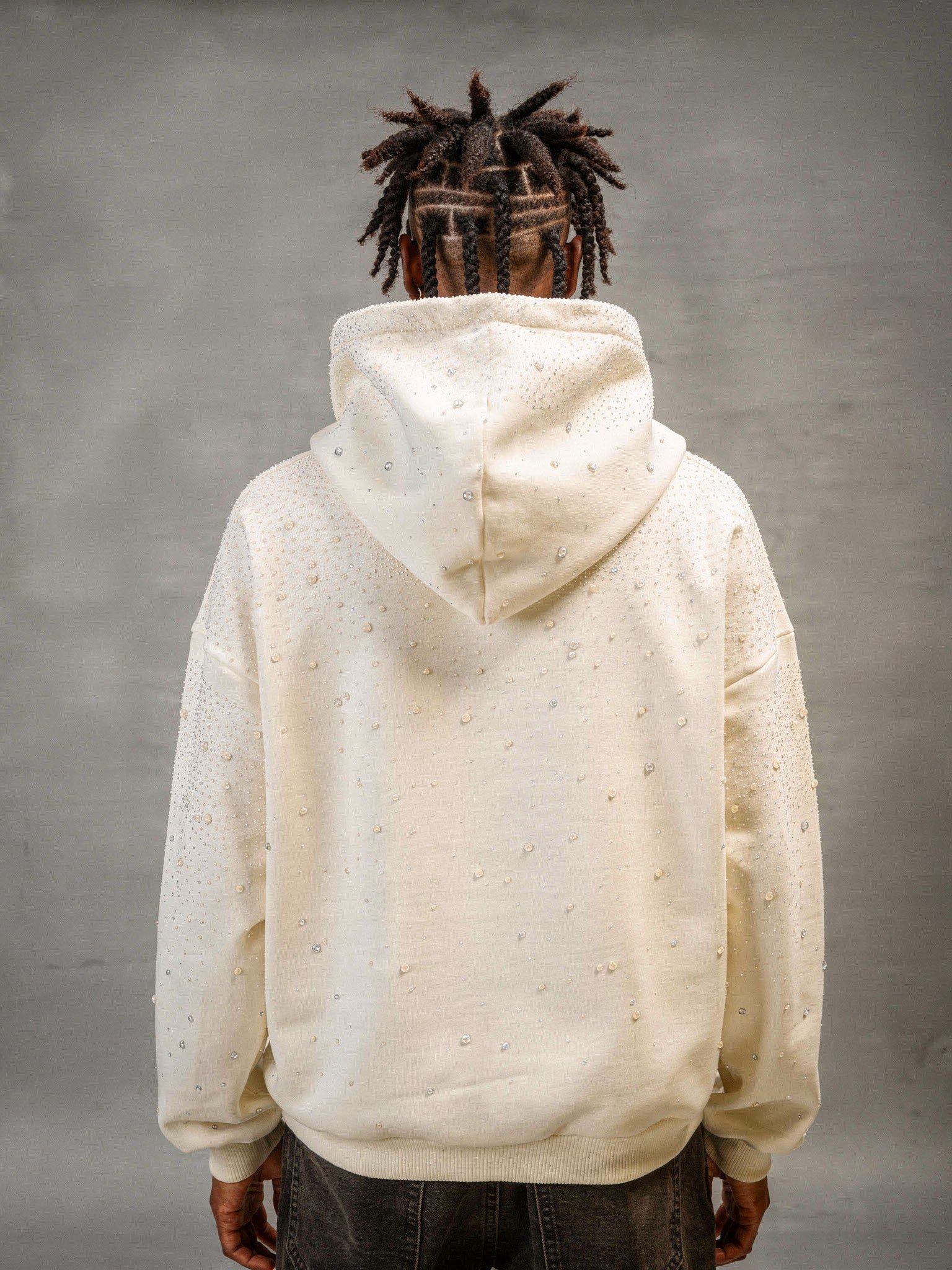 Model trägt Rhinestone Hoodie in cream weiß von Gabriel Abera. Die Ansicht ist von hinten.