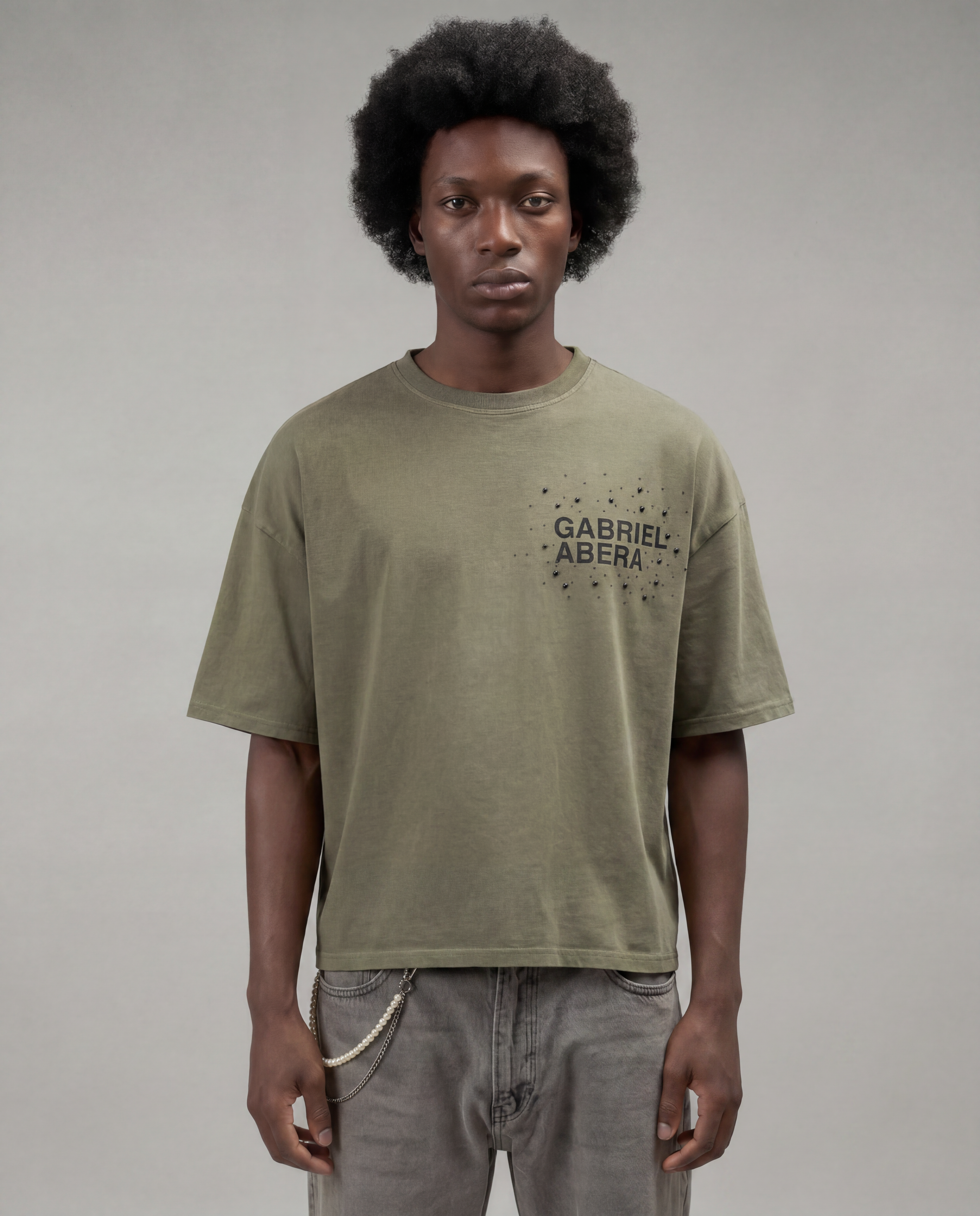 Male model with afro wearing the Gabriel Abera Rhinestone Logo Tee in olive – oversized fit, front view, rhinestone 'Gabriel Abera' logo on chest, grey background