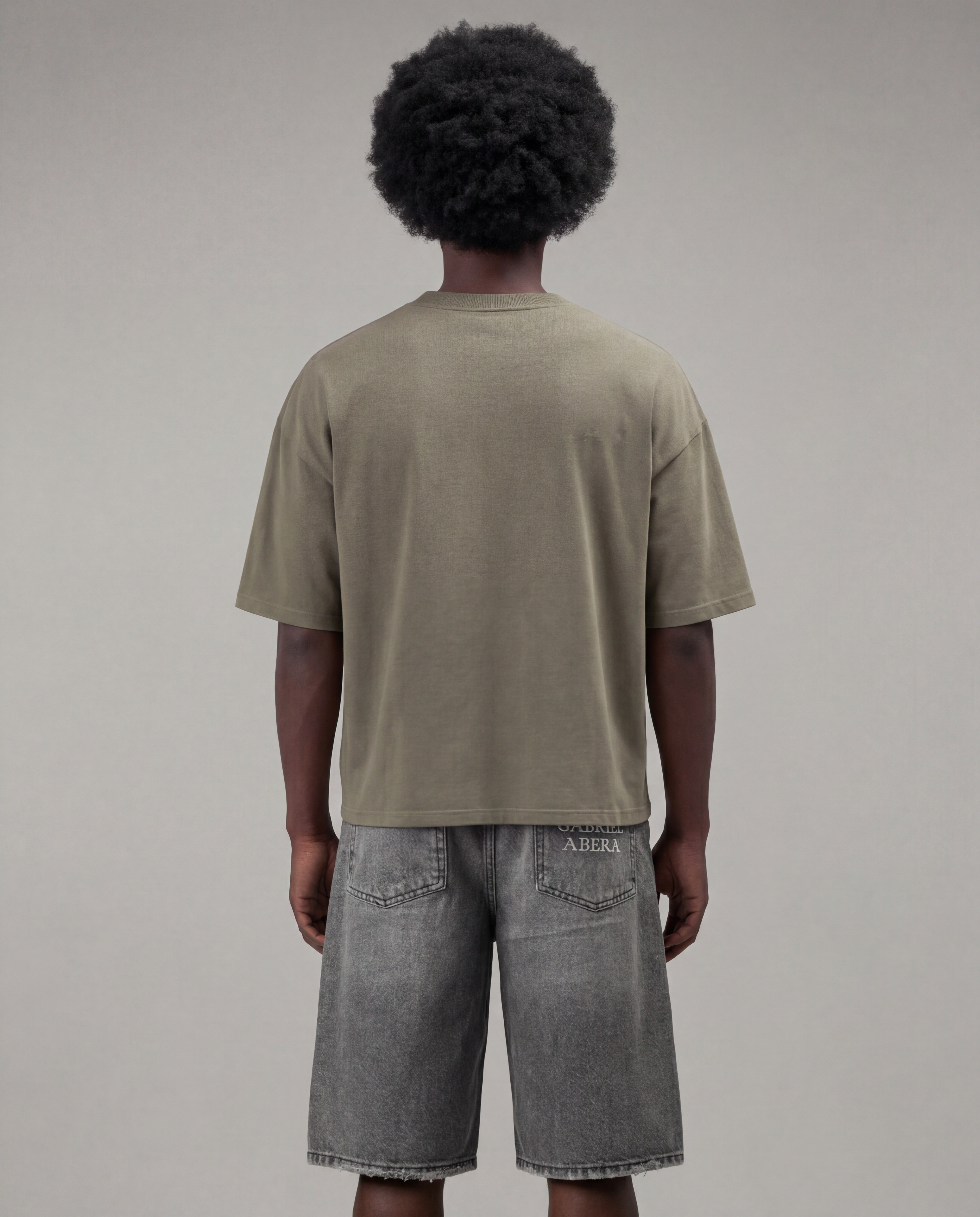 Female model wearing the Gabriel Abera Rhinestone Logo Tee in olive – front view, styled with denim shorts, relaxed streetwear look, grey background