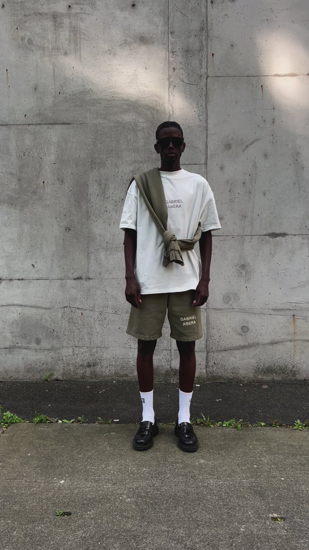 Video of model wearing GA T-Shirt in cream white with khaki logo, walking and turning to showcase relaxed fit and cotton texture