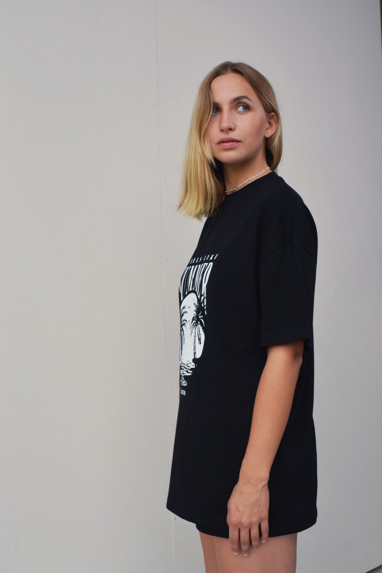 Female model wearing a Black oversize tshirt with round white summer design on the front 