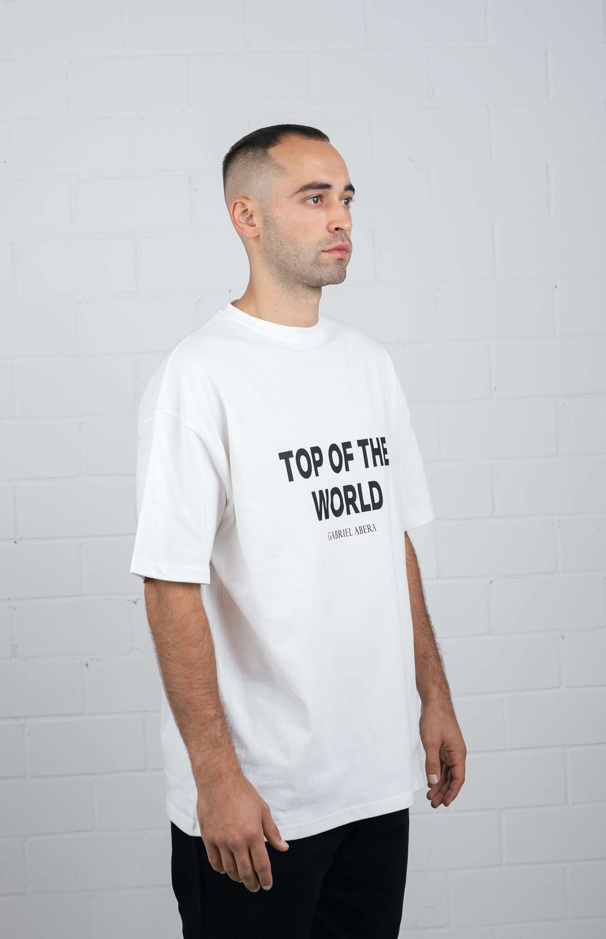 Male model wearing a White oversize tshirt wiht black top of the world design in the front
