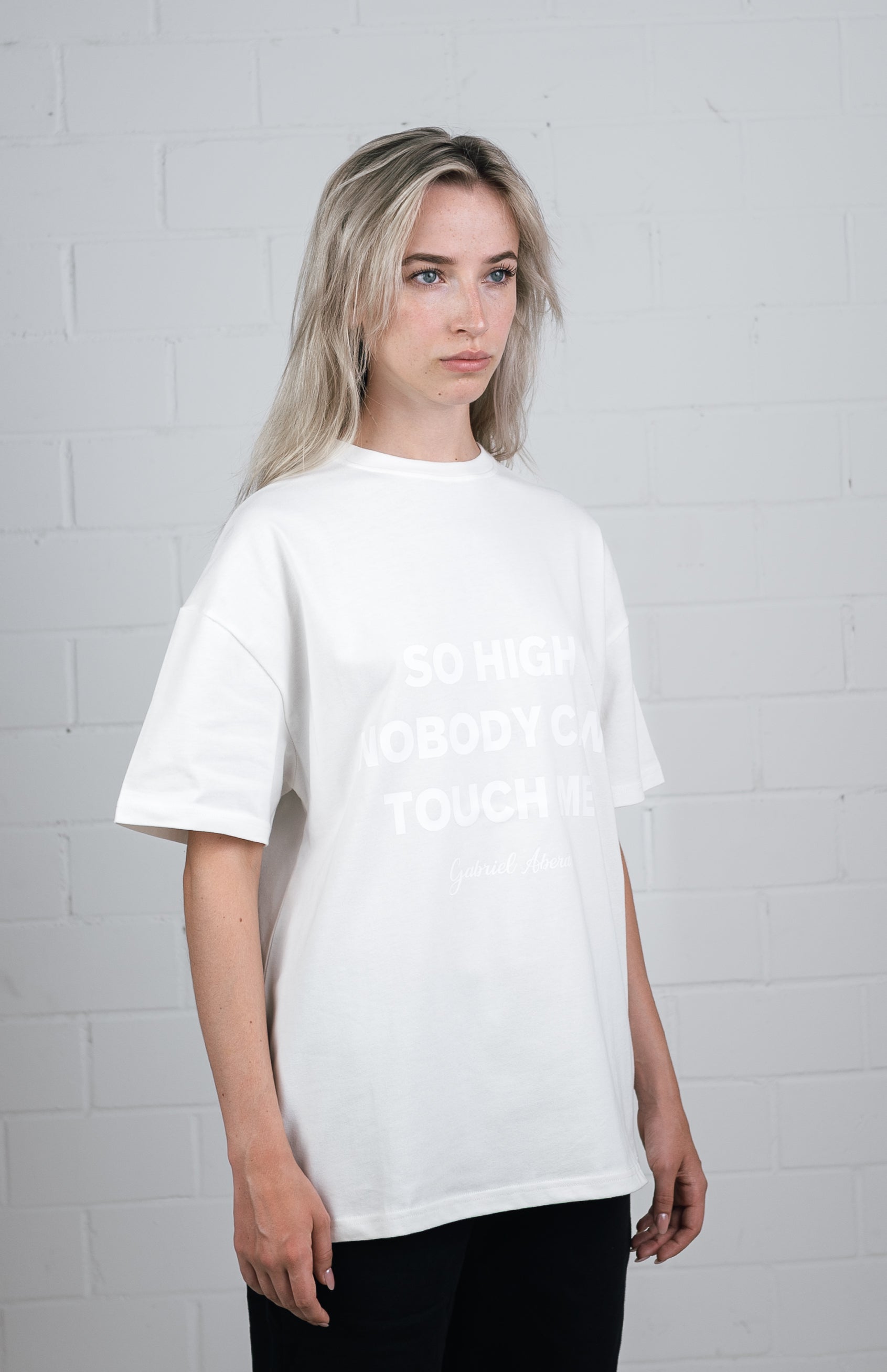 Female model wearing a White oversize tshirt with white so high nobody can touch me design in the front