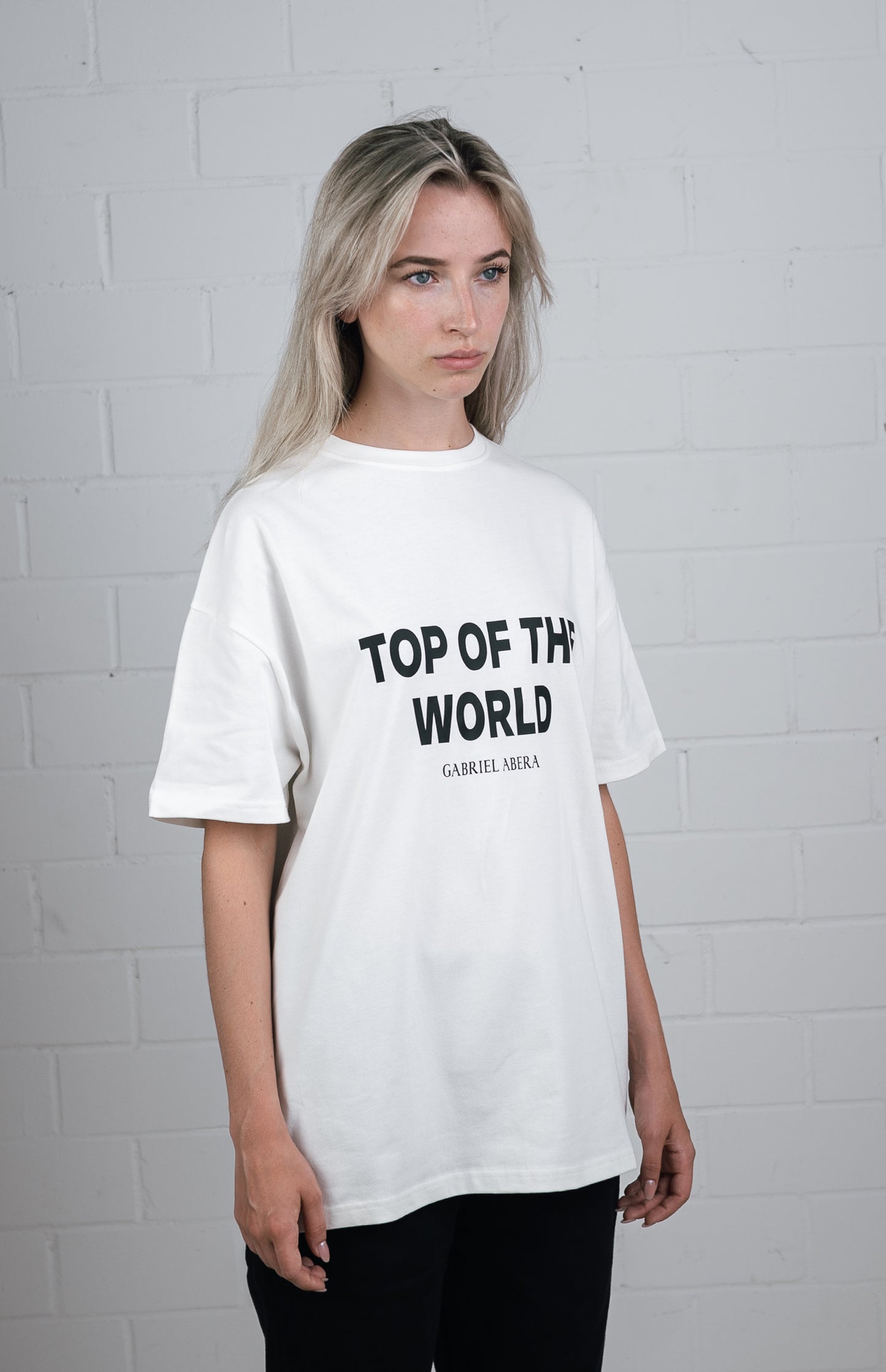 Female model wearing a White oversize tshirt with black top of the world design in the front