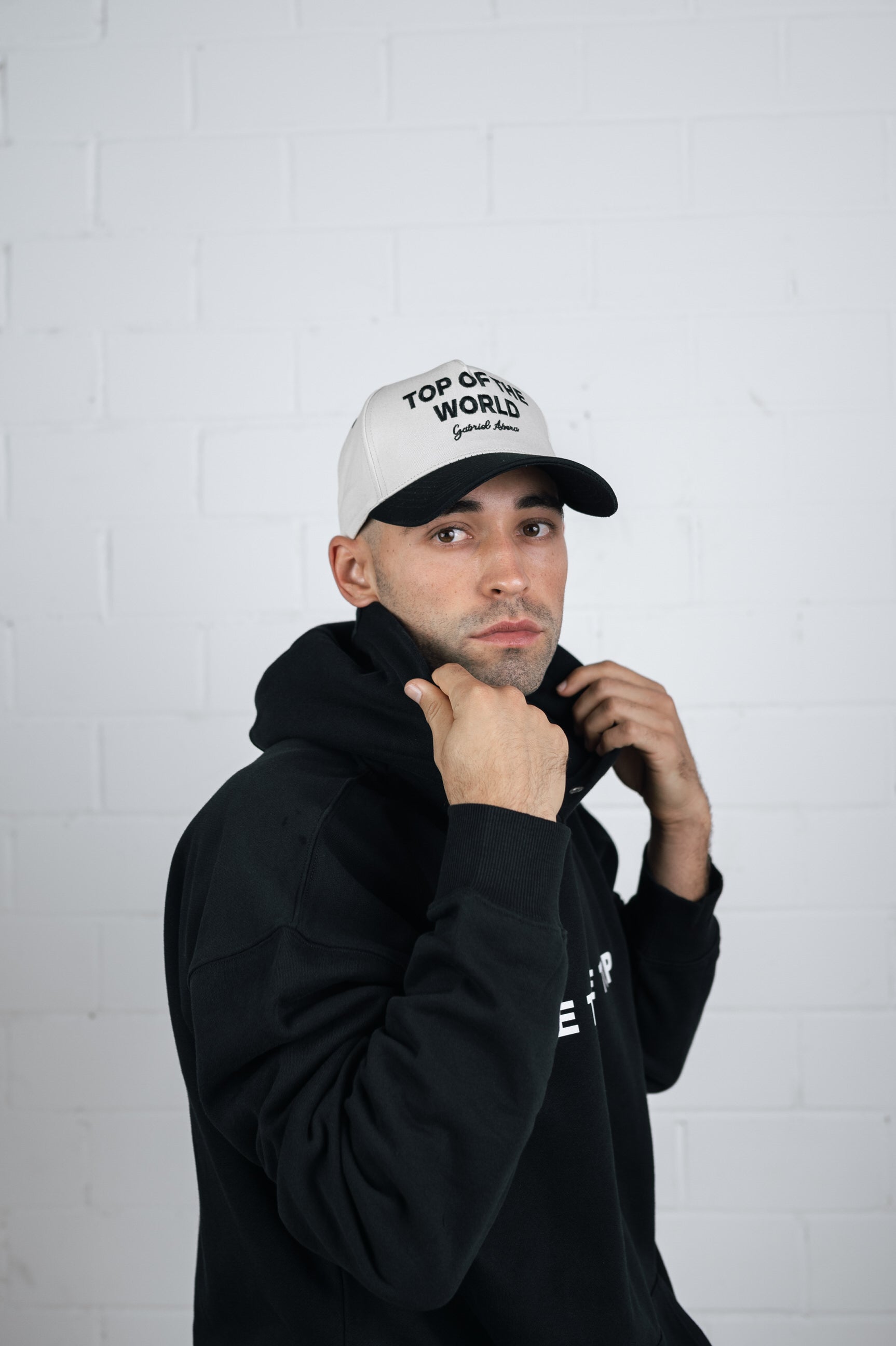 Male model wearing a White cap with black shield and black top of the world embroidery in the front 