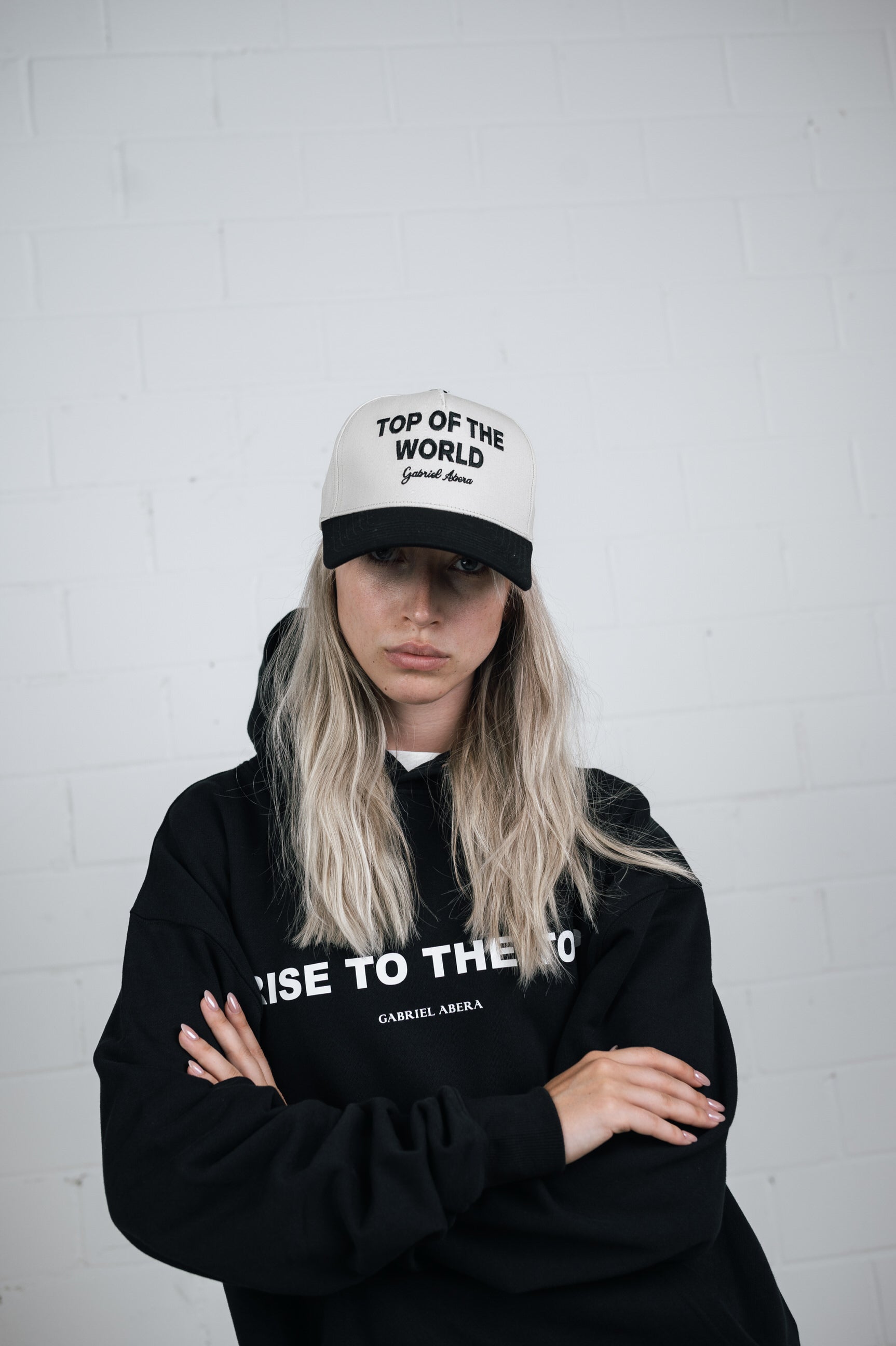 Female model wearing a White cap with black shield and black top of the world embroidery in the front 