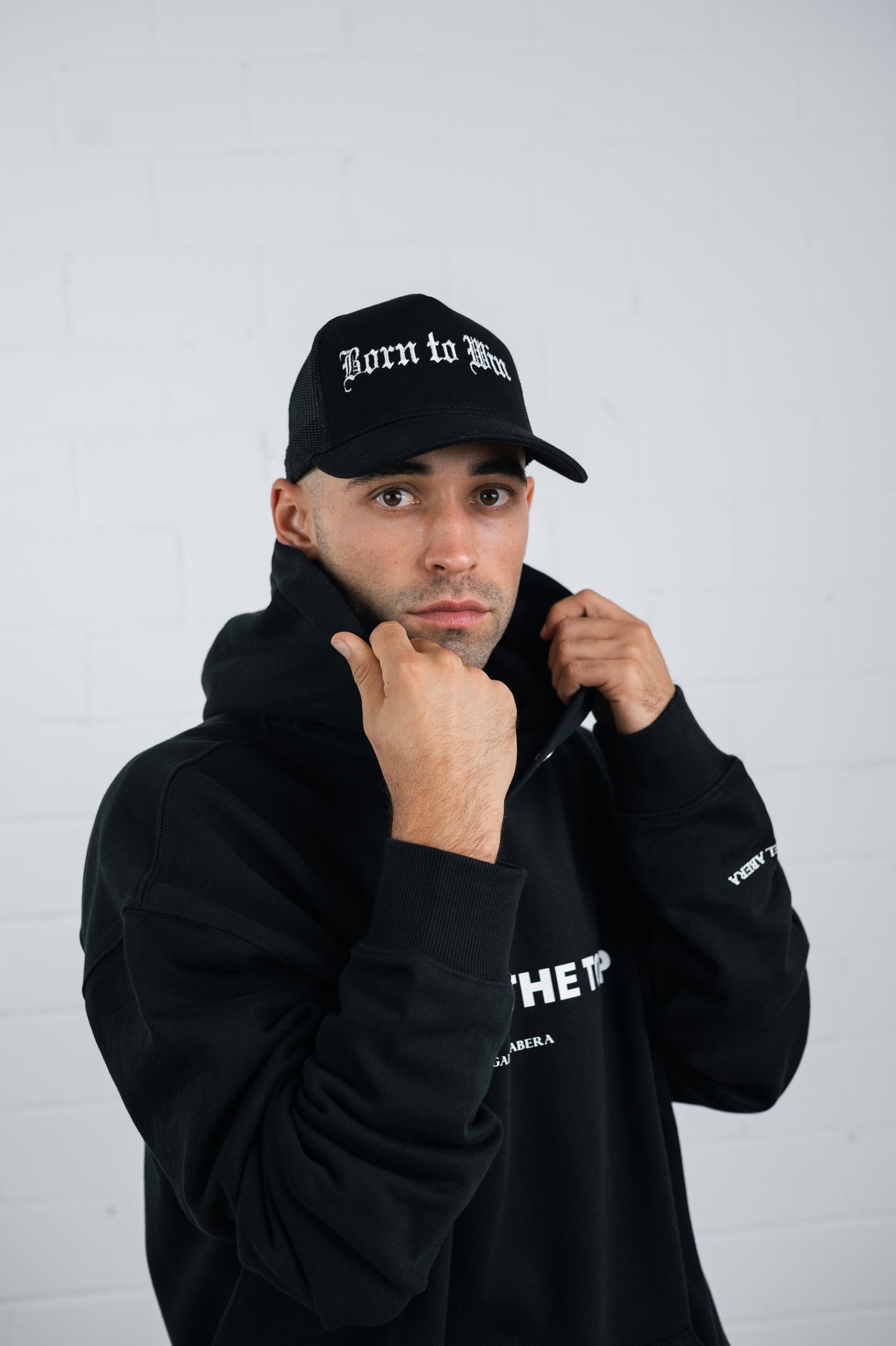Male model wearing a Black trucker cap with born to win embroidery