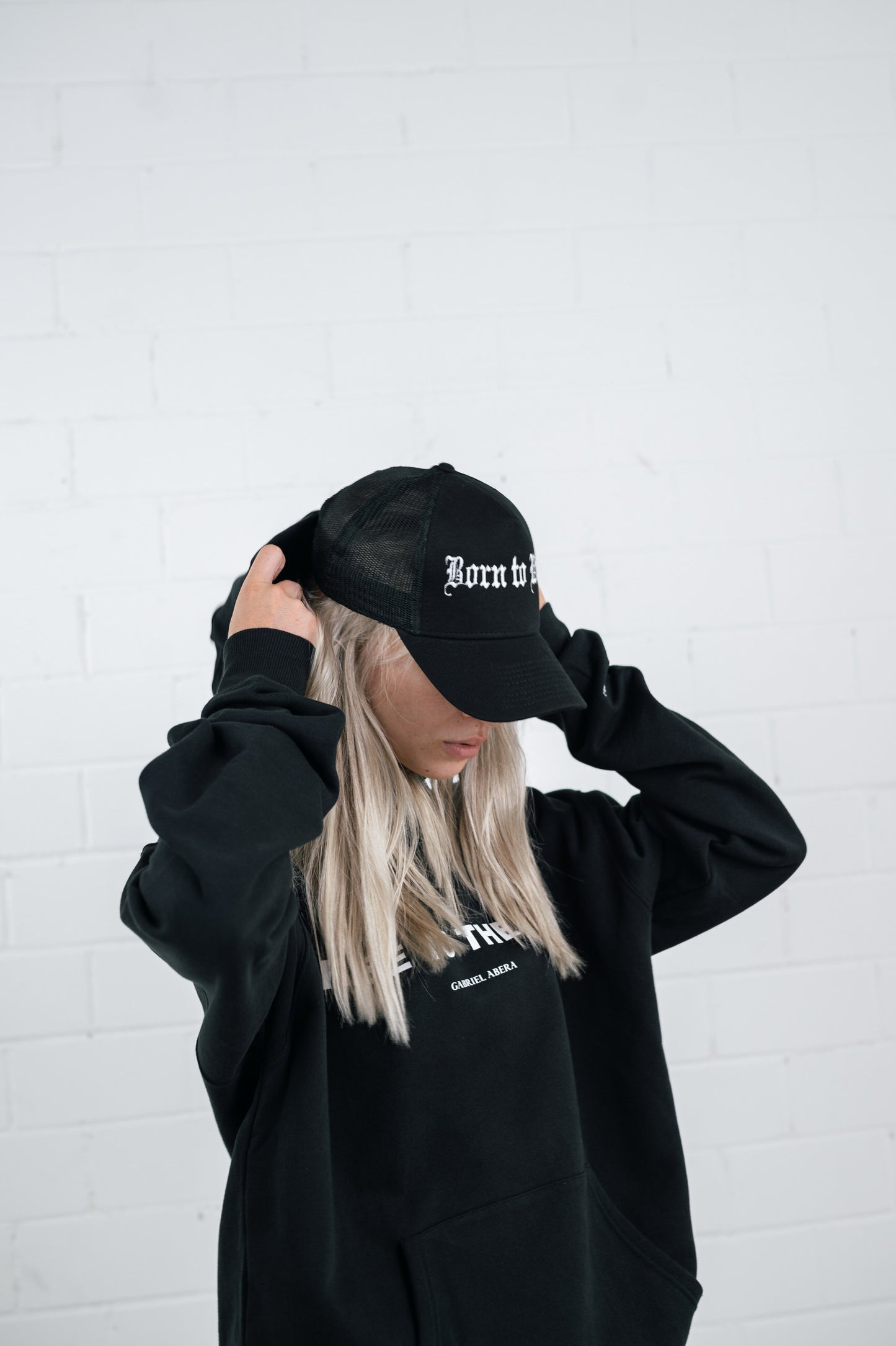 Female model wearing a Black trucker cap with born to win embroidery