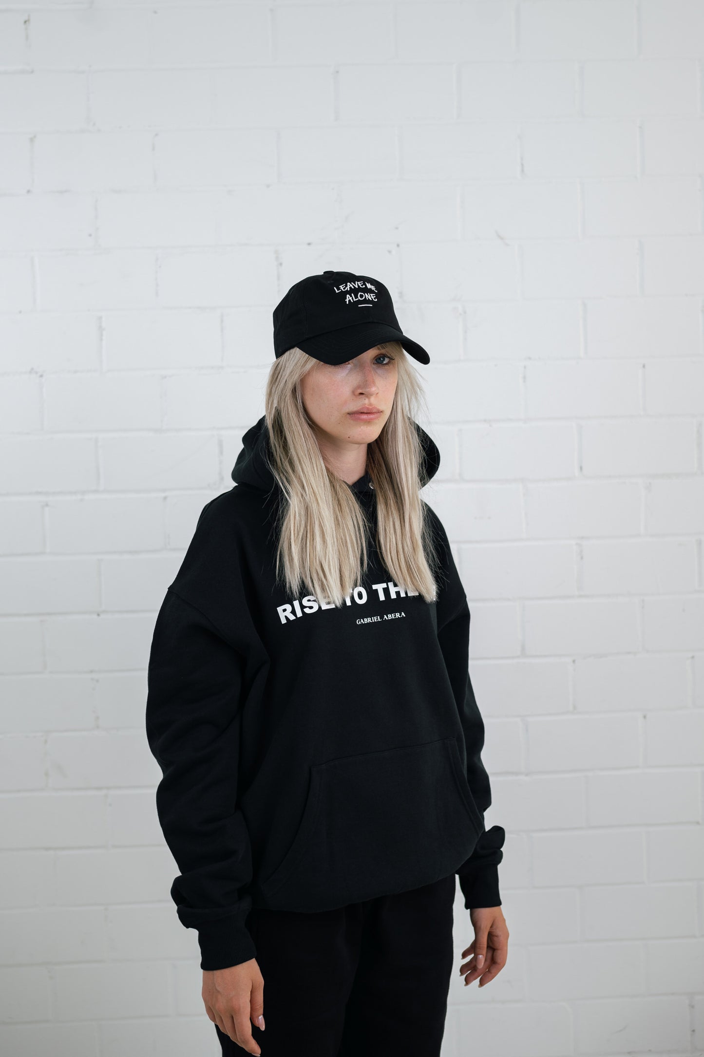 Female model wearing a Black cap with white leave me alone embroidery in the front