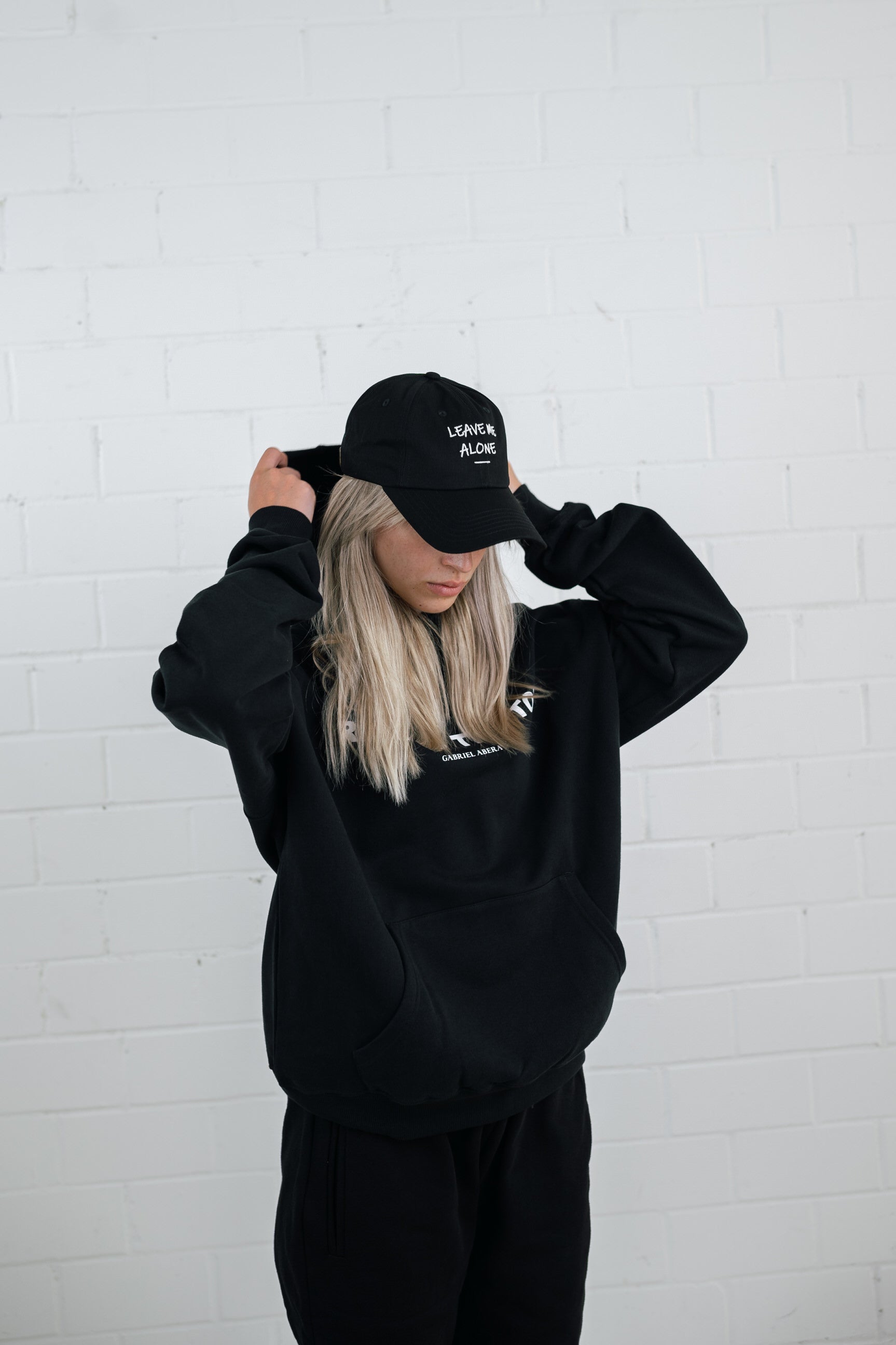 Female model wearing a Black cap with white leave me alone embroidery in the front