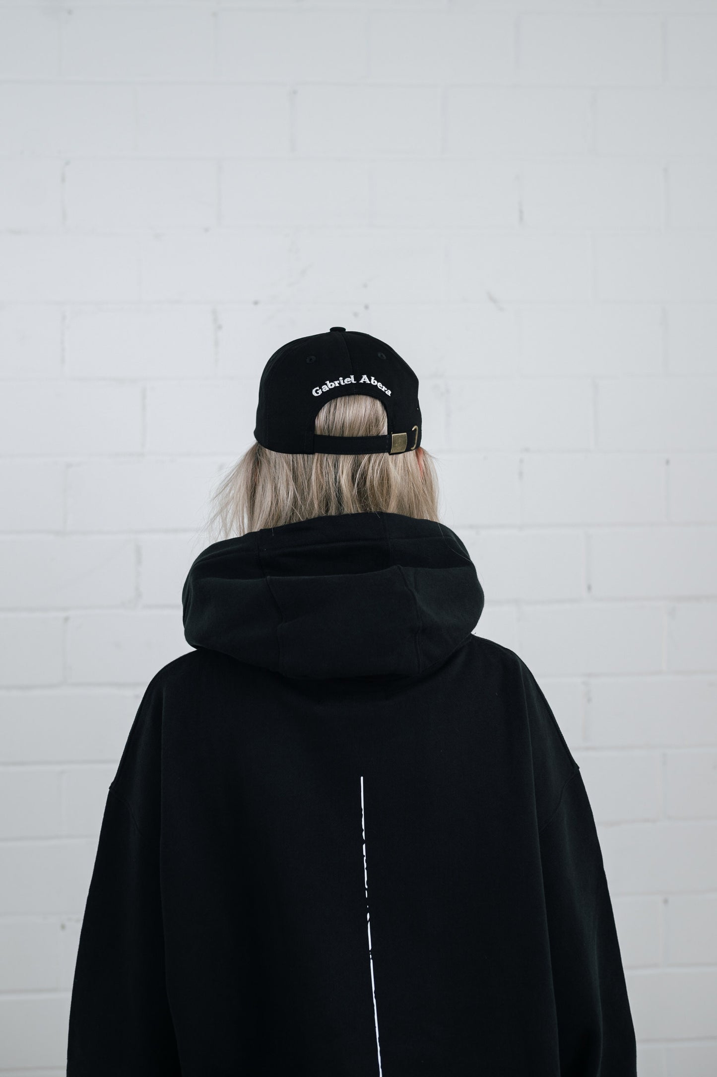 Female model wearing a Black cap with white brand name embroidery on the back