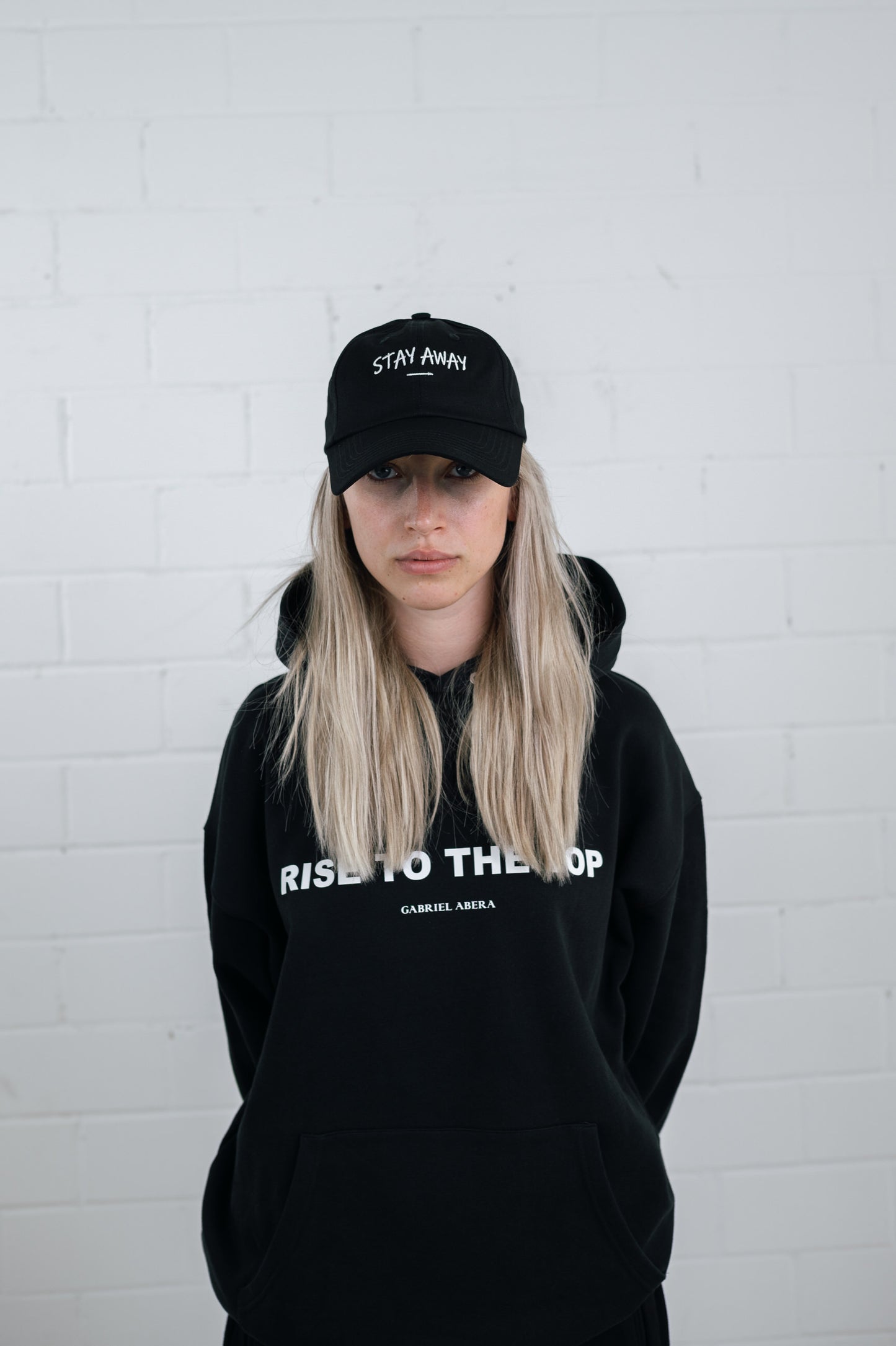 Female model wearing a Black cap with white stay away embroidery