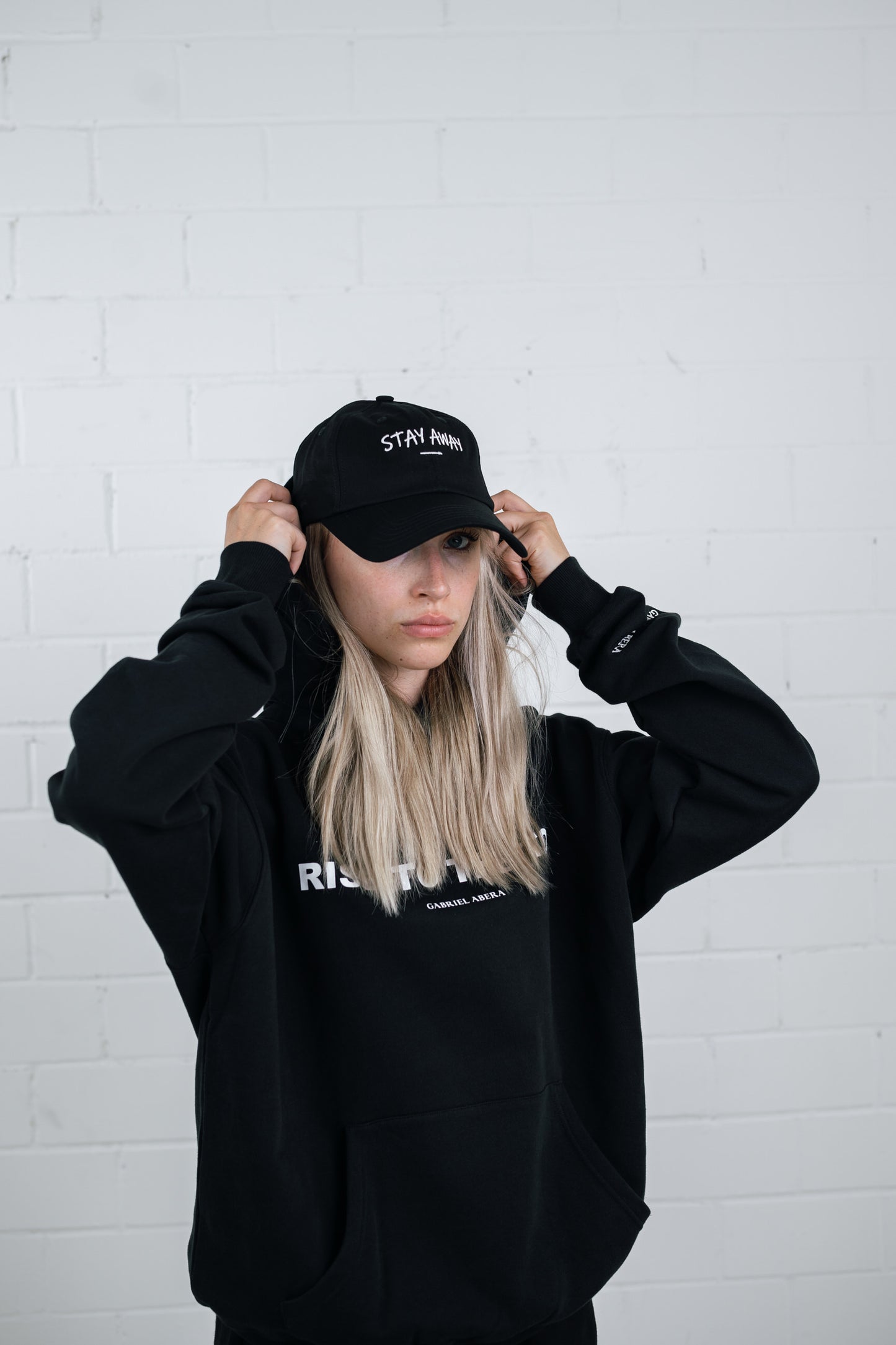 Female model wearing a Black cap with white stay away embroidery