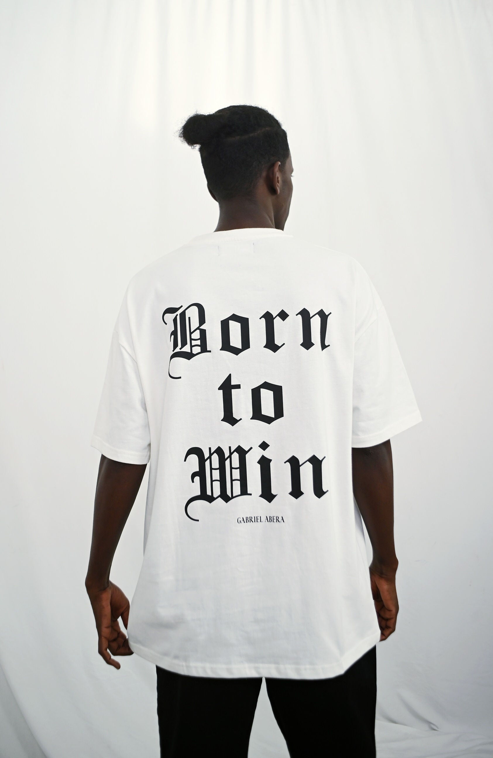 Male model wearing a white oversize Tshirt with born to win design o nthe back