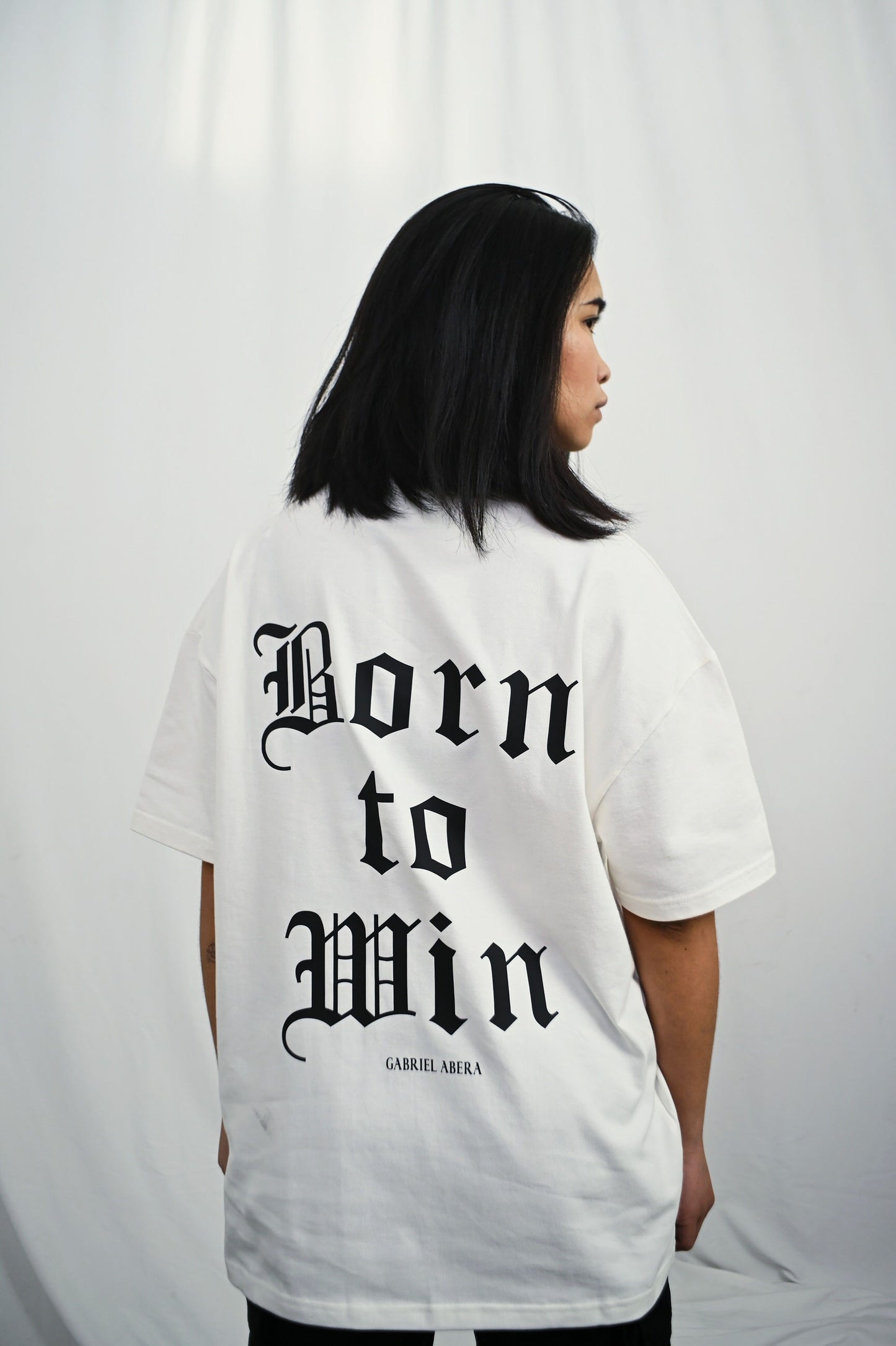 Female model wearing a white oversize Tshirt with born to win design o nthe back