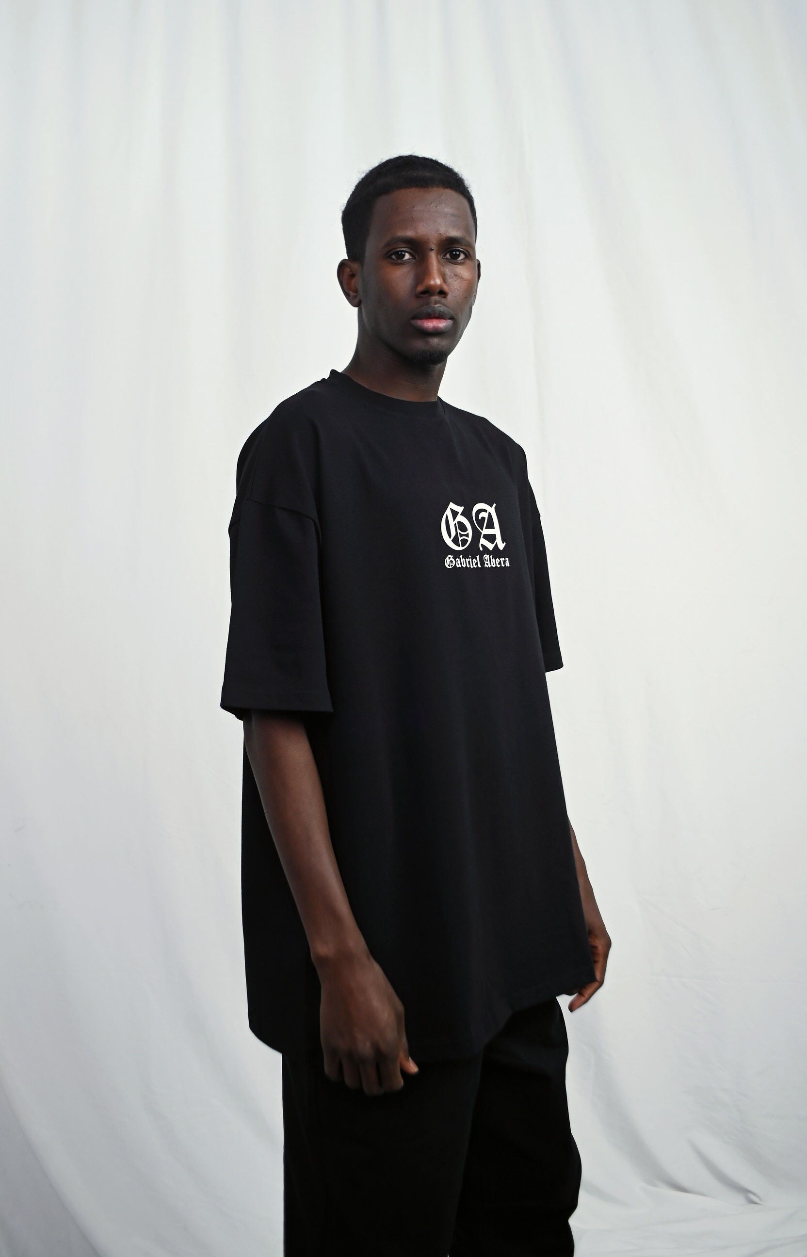 Male model wearing s Black oversize Tshirt with brand design on the front