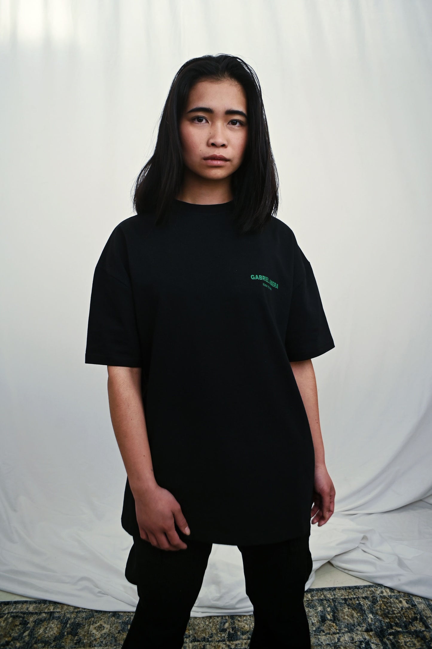 Female model wearing a Black oversize tshirt with green brand design on the front